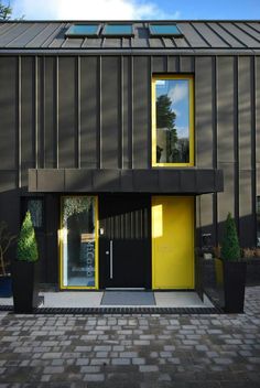 a black building with two yellow doors and some potted plants on the side walk