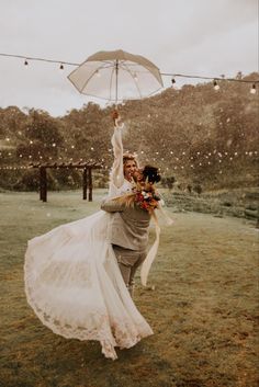 a bride and groom are dancing in the rain with an umbrella over their heads as they dance