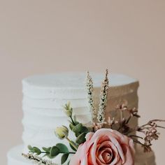 a white wedding cake with pink flowers and greenery on the top, against a pale background