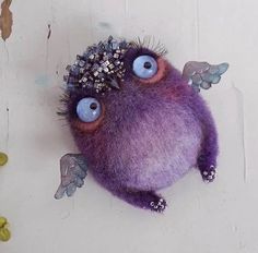 a purple stuffed animal with blue eyes and wings on it's head is hanging from a white wall