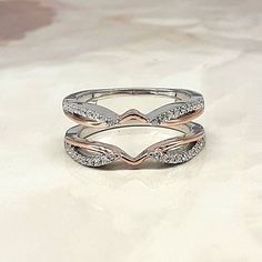 two white gold wedding rings with diamonds on top of each other, sitting on a marble surface