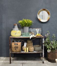 a table with some plants and other items on it next to a wall that has a mirror above it