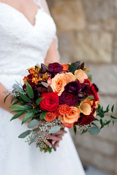 a bridal holding a bouquet of red and orange flowers with greenery on it