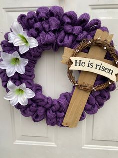 a purple wreath with white flowers and a cross on the front door that says he is risen