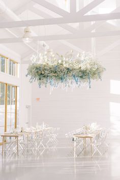 a room filled with lots of tables covered in white flowers and hanging chandelier