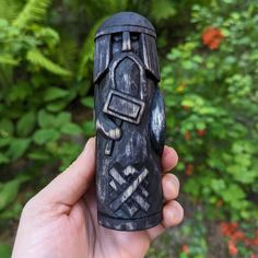 a hand holding a carved wooden object in front of some bushes