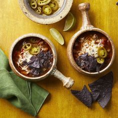 two bowls filled with chili, olives and tortilla chips on top of a wooden table