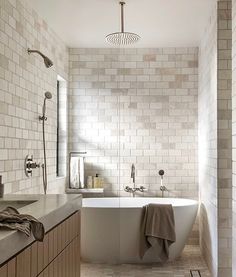 a white bath tub sitting next to a sink under a window in a bathroom with tiled walls