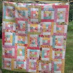 a quilt hanging from a clothes line in a yard with grass and trees behind it