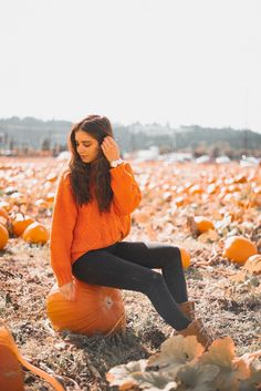 a woman sitting on top of a pumpkin patch with her hands in her hair and wearing an orange sweater