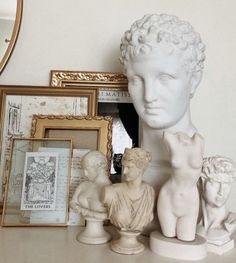 there is a white busturine on the table with other statues and framed pictures