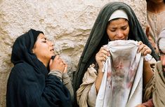 two women are looking at a cloth hanging on a hook and another woman is wearing a headscarf