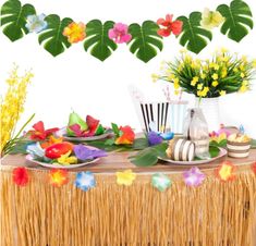 the table is set with flowers and plates on it, along with tropical leaves hanging from the ceiling