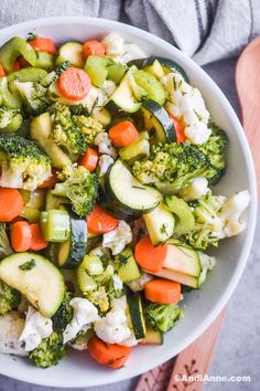 a white bowl filled with vegetables on top of a wooden table next to utensils