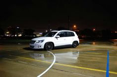 a white car is parked in an empty parking lot at night with its lights on