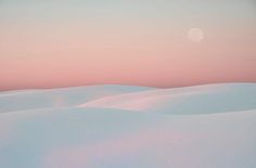 the moon is setting over an expanse of white snow covered hills and plaines in the distance