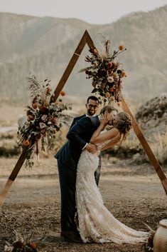 a bride and groom kissing in front of an arch made out of wood sticks with flowers