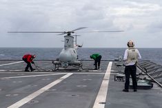 two men are working on the deck of an aircraft carrier while another man stands nearby