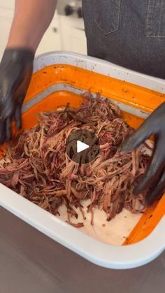 a person in black gloves and rubber gloves scooping shredded food into a white container