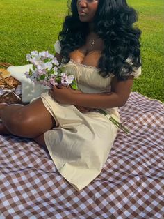 a woman sitting on top of a checkered blanket with flowers in her hand and wearing a white dress