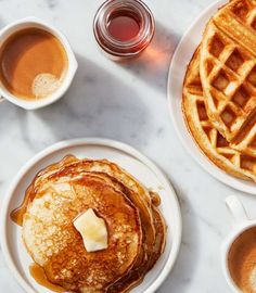 two plates with pancakes and syrup on them next to cups of coffee, butter and syrup