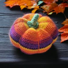 a crocheted pumpkin sitting on top of a wooden table next to autumn leaves