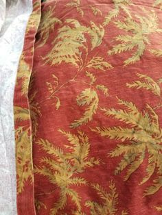 an old red and gold bed spread on top of a white pillow cover with yellow leaves