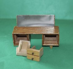 a miniature wooden desk with a mirror and drawer on it's side, sitting on a green surface