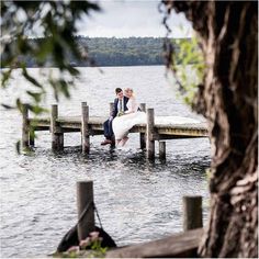 a bride and groom sitting on a dock in the water