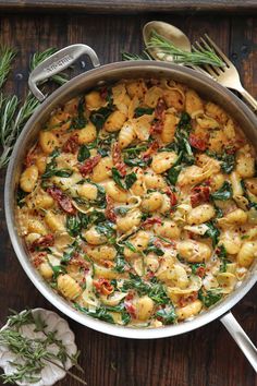 a pot filled with pasta and spinach on top of a wooden table next to utensils