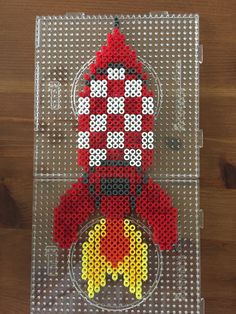 a red and yellow toy sitting on top of a clear plastic tray covered in beads