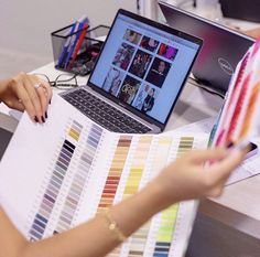 a woman sitting at a desk with a laptop and color swatches