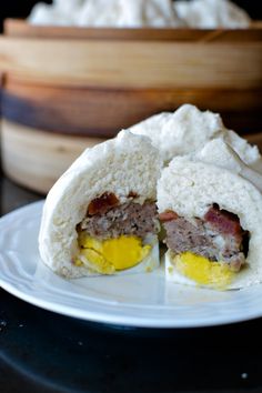 an egg and meat sandwich on a white plate next to a wooden container with eggs in it