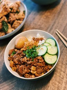 two bowls filled with food sitting on top of a wooden table next to chopsticks