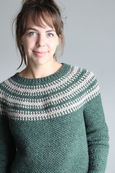 a woman wearing a green sweater with white and grey stripes on it, smiling at the camera