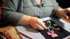 a woman is working with clay flowers on a piece of black paper that she made