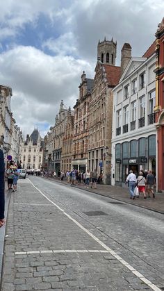 people are walking down the street in an old european city with tall buildings and cobblestone streets