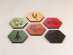 four wooden coasters with different designs on them sitting on a white surface, one has an animal and the other has a pine tree