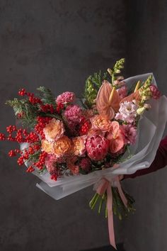 a woman holding a bouquet of flowers in her hand with red berries and greenery