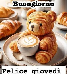 a teddy bear sitting on top of a plate next to a cup of coffee and croissants