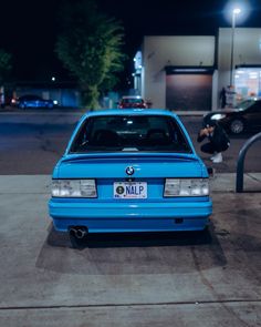 a blue bmw is parked in front of a gas station at night with its hood up