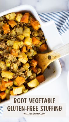 a white casserole dish filled with vegetables and meat, topped with a wooden spoon