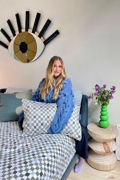 a woman sitting on top of a bed in front of a wall mounted eyeball clock