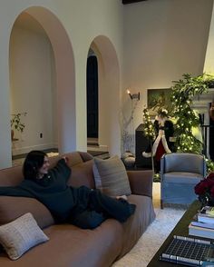 a woman laying on top of a couch in a living room next to a christmas tree