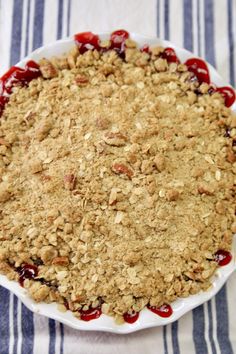 a pie with crumbs and cherries on top in a white dish sitting on a striped table cloth