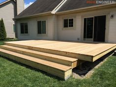 a wooden deck in front of a house with grass on the ground and two steps leading up to it