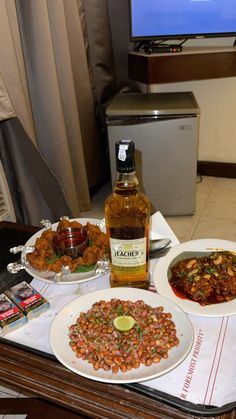 a table topped with plates of food next to a bottle of alcohol and a tv