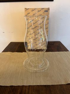 a clear vase sitting on top of a wooden table next to a piece of paper