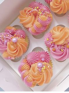 six cupcakes with pink and orange frosting in a white box on a table