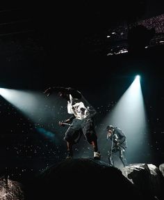 two men performing on stage with spotlights in the background and one man holding an umbrella